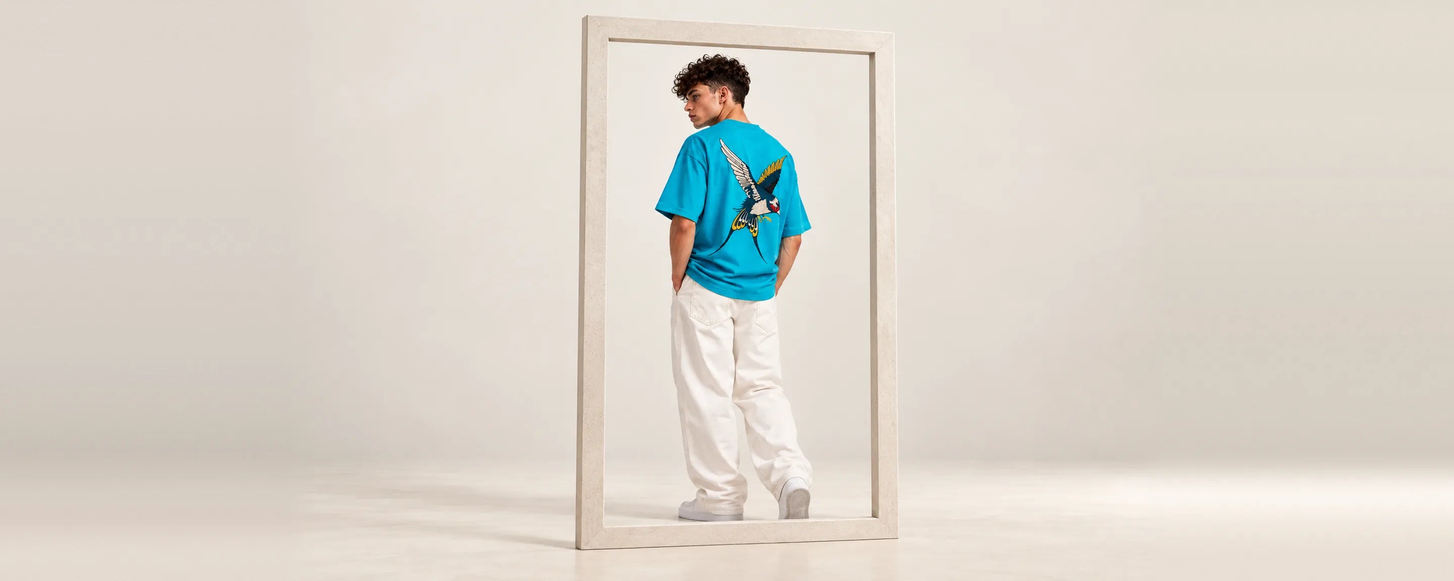 AEROKORA campaign: oversized turquoise tee with a bird print, framed in a pale studio