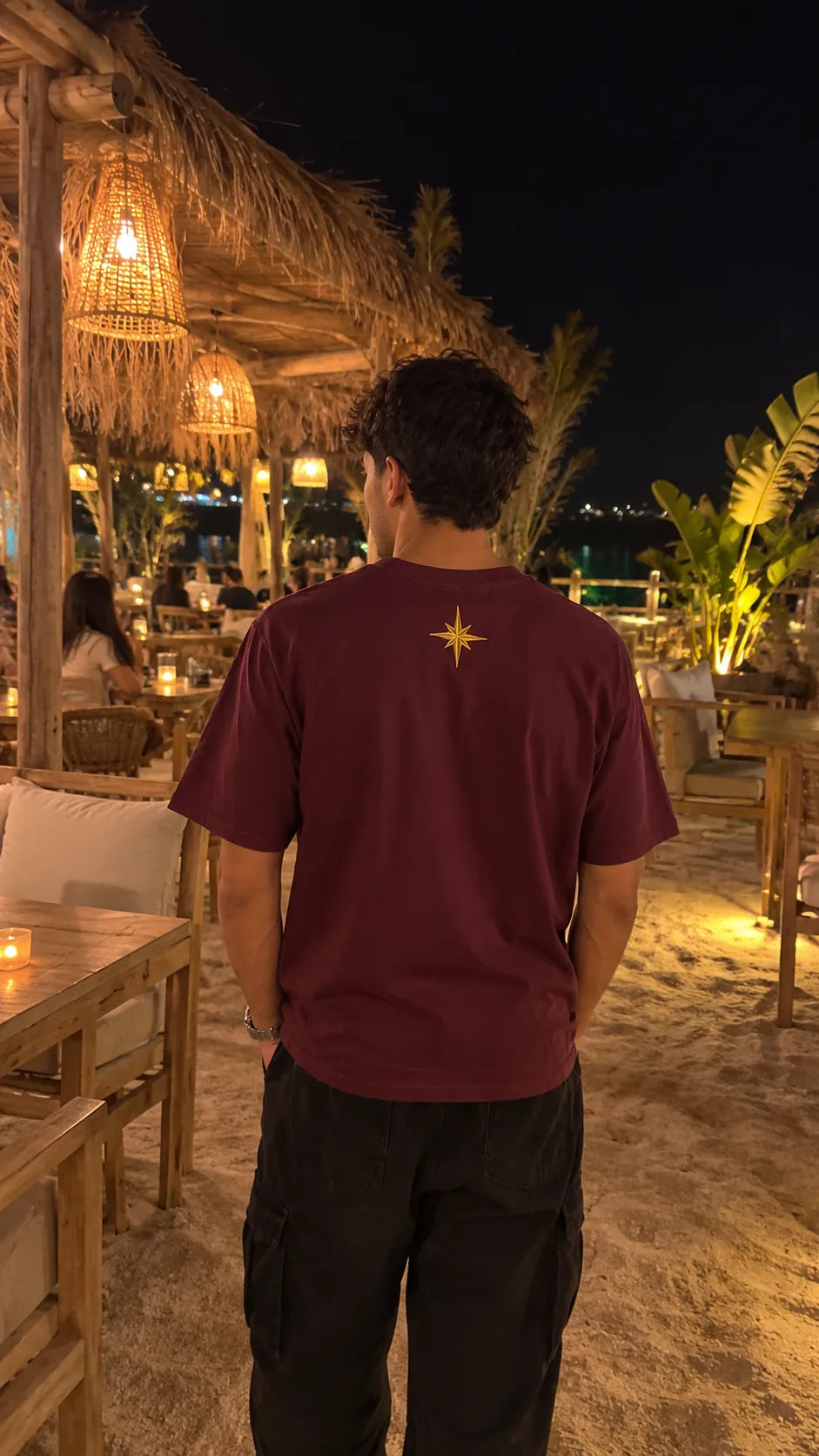 Back view of a maroon tee with a gold star motif at a beach bar at night