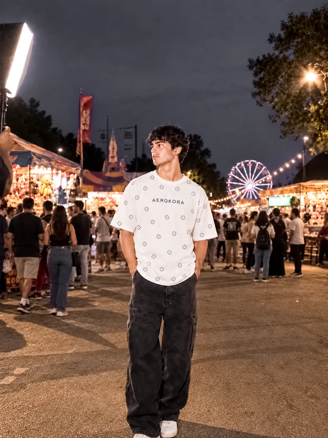 White AEROKORA pattern tee and black jeans at a night fair with a lit Ferris wheel