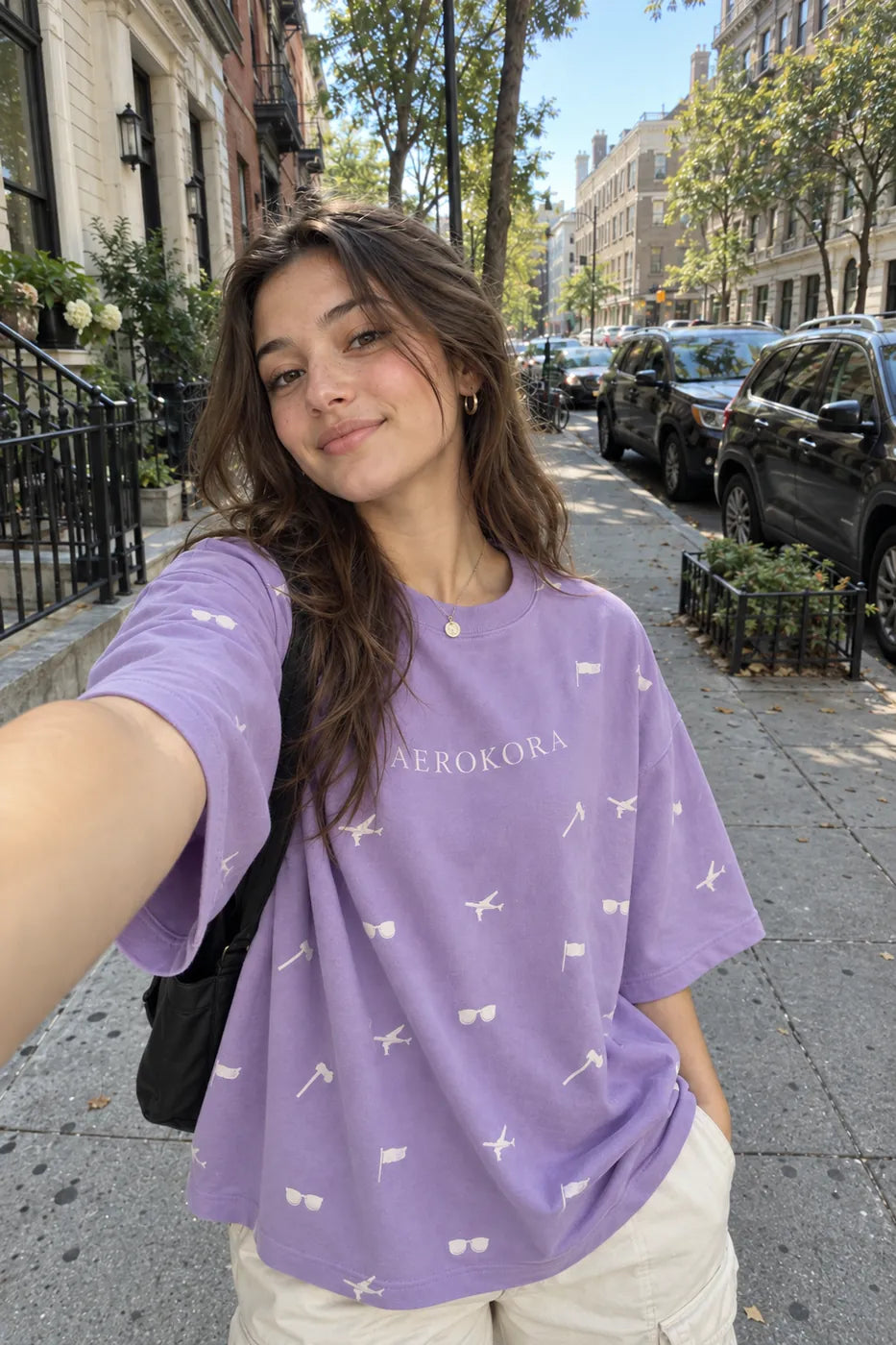 Street selfie in an oversized lavender AEROKORA tee on a sunny brownstone block