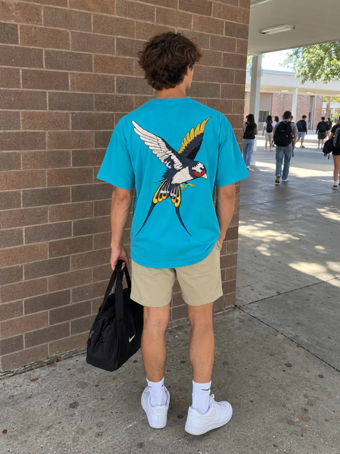 Back view of a turquoise tee with a large bird graphic in a courtyard